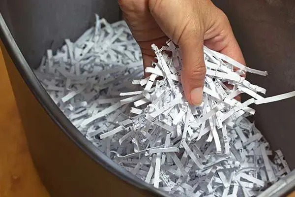 A hand holding a bunch of shredded paper over a waste bin.