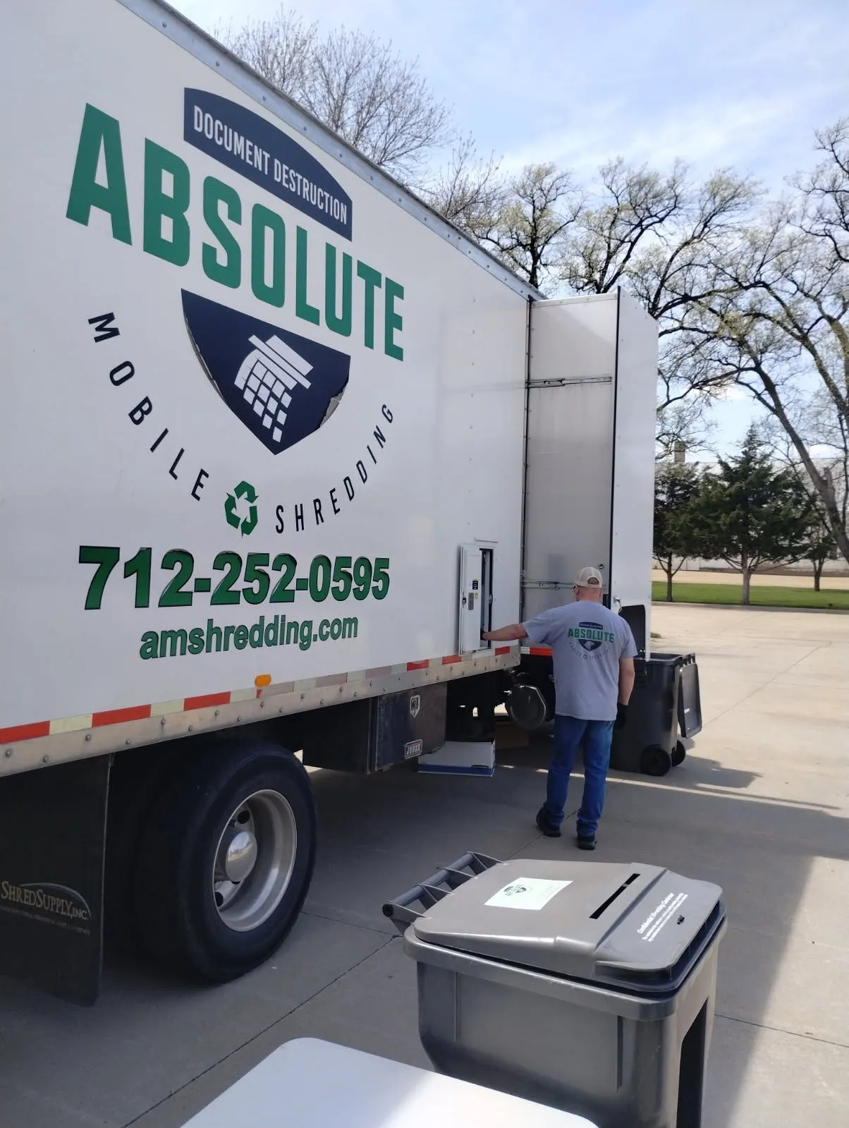 A worker in an Absolute Mobile Shredding shirt loads documents into a secure shredding truck.